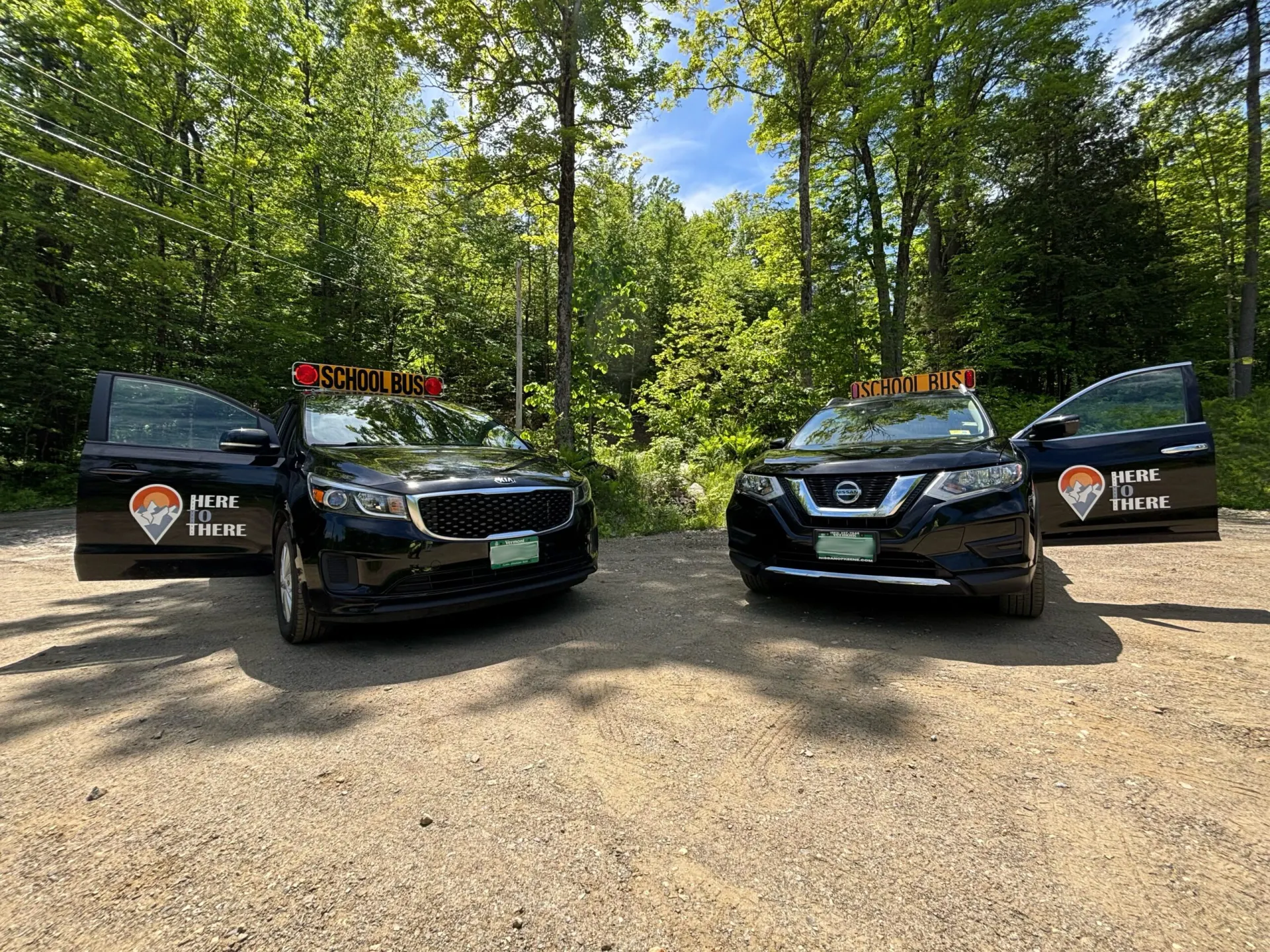 Two Here to There school-bus-certified vehicles parked in the woods, doors open